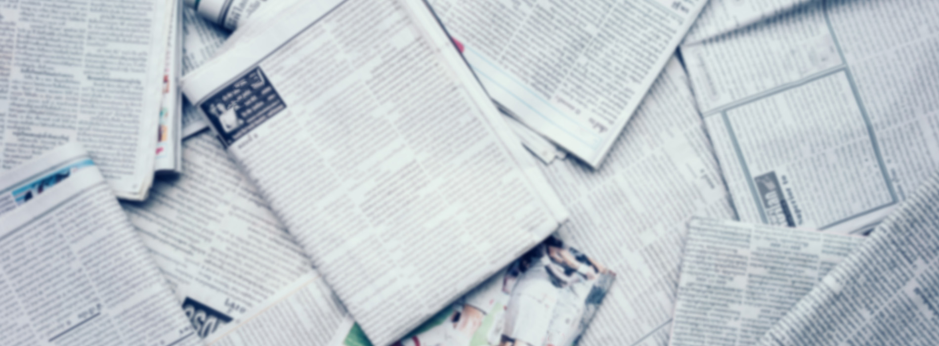 The image shows a collection of newspapers scattered on a surface, with some papers partially obscured by others.