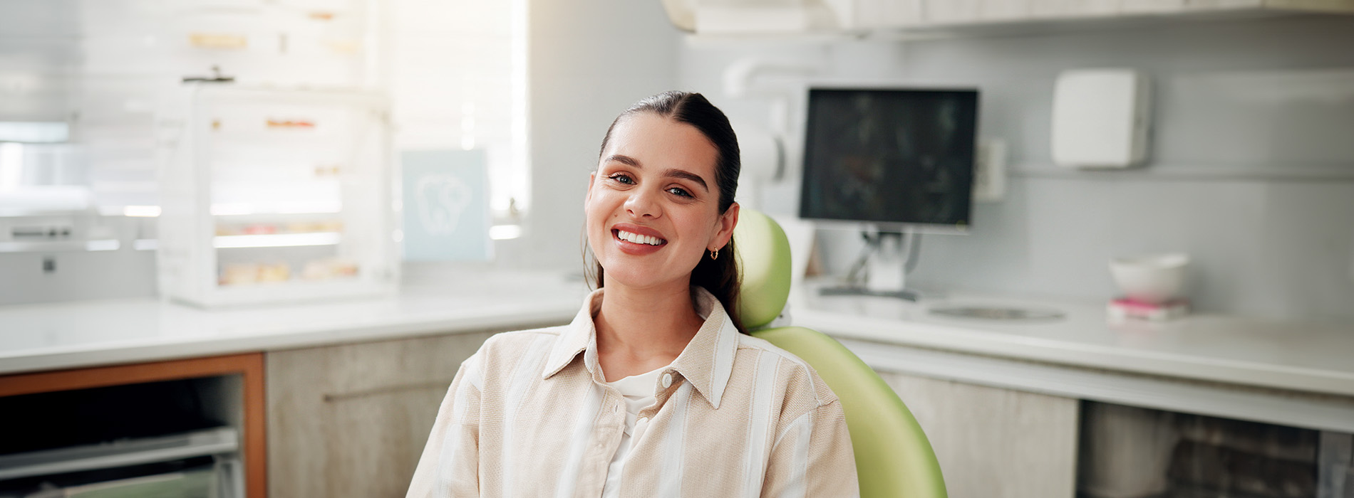 The image shows a person sitting on a green chair with a smile, set against a blurred background of a kitchen interior.